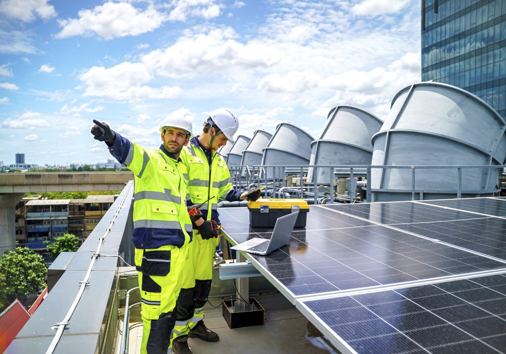 Two technicians in bright safety gear work on solar panels while discussing their project.